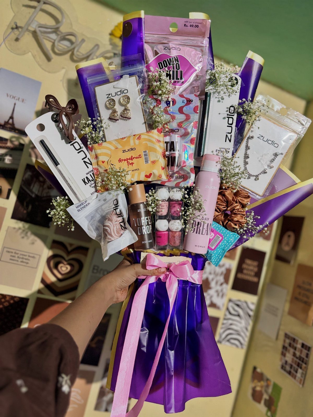 Gift bouquet with beauty products and jewelry wrapped in purple and gold paper.