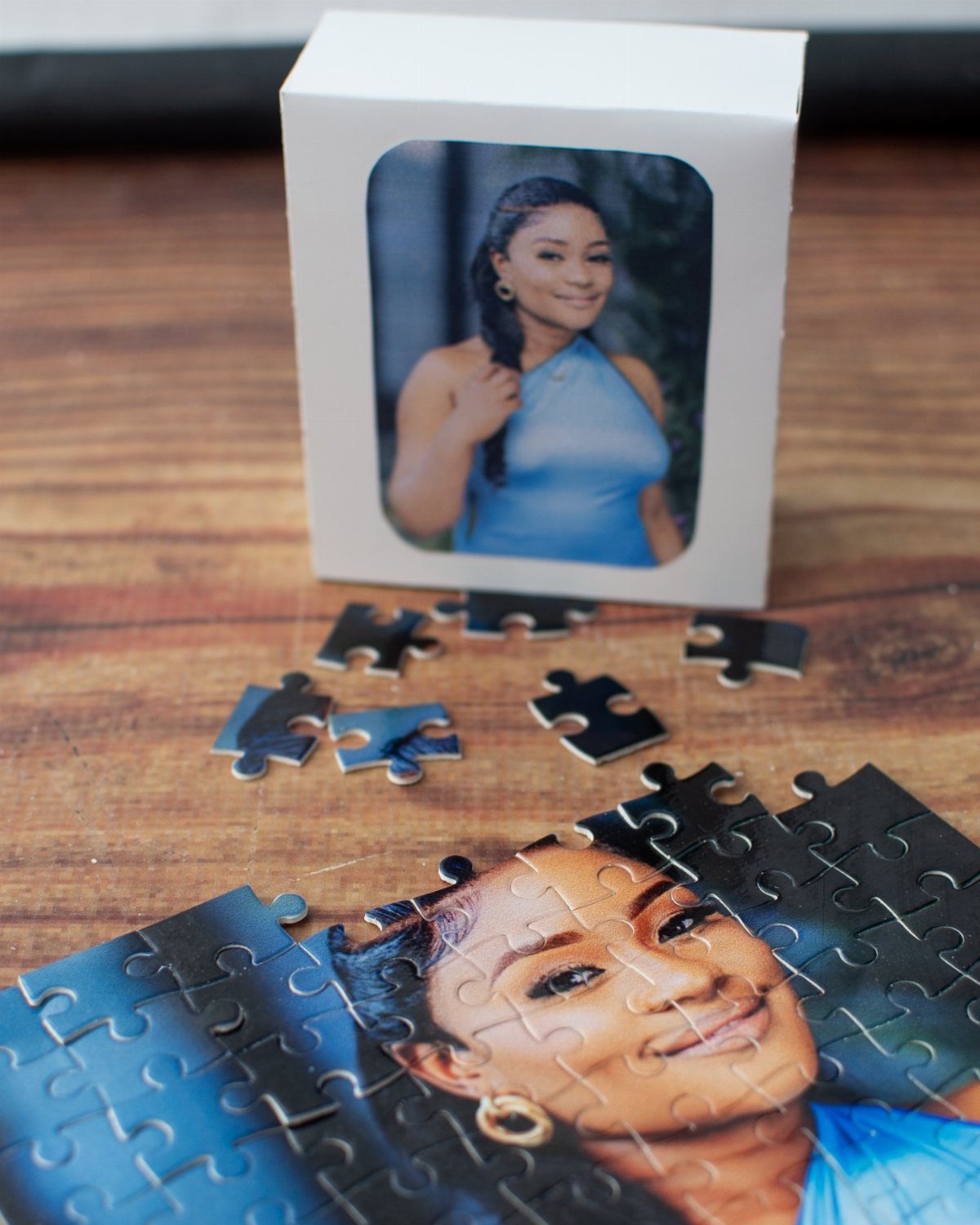 Partially completed photo puzzle of a woman with a reference box on wood.