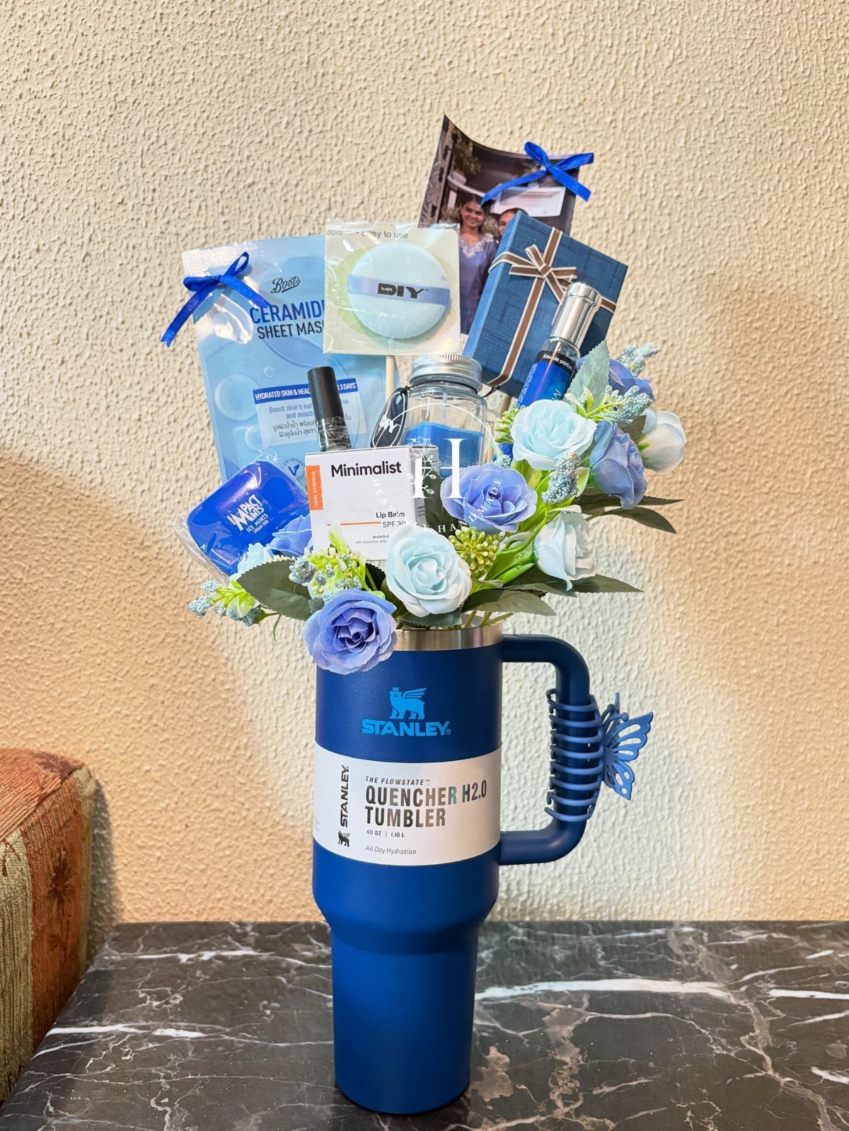 Blue Stanley tumbler filled with light blue roses and various skincare gift items.