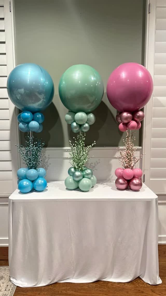 Three colorful balloon centerpieces in blue, green, and pink on a white table.