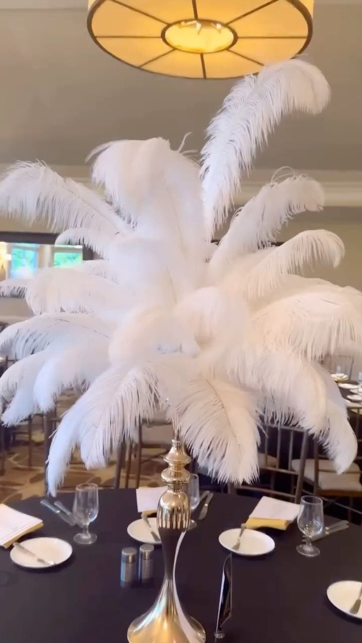 White ostrich feather centerpiece in a gold vase on a black banquet table