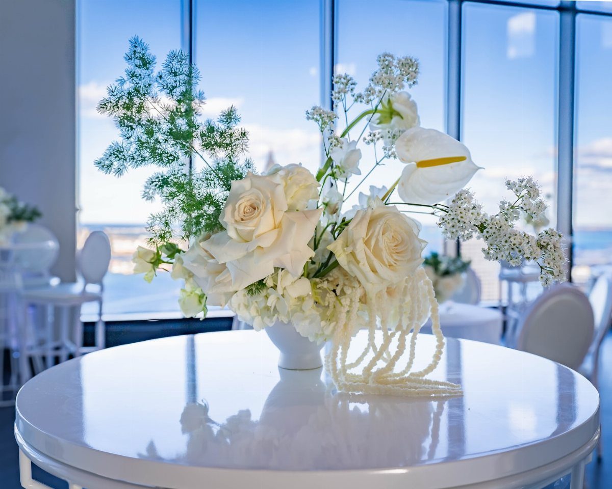 White floral arrangement with roses and pearls on a glossy white table.