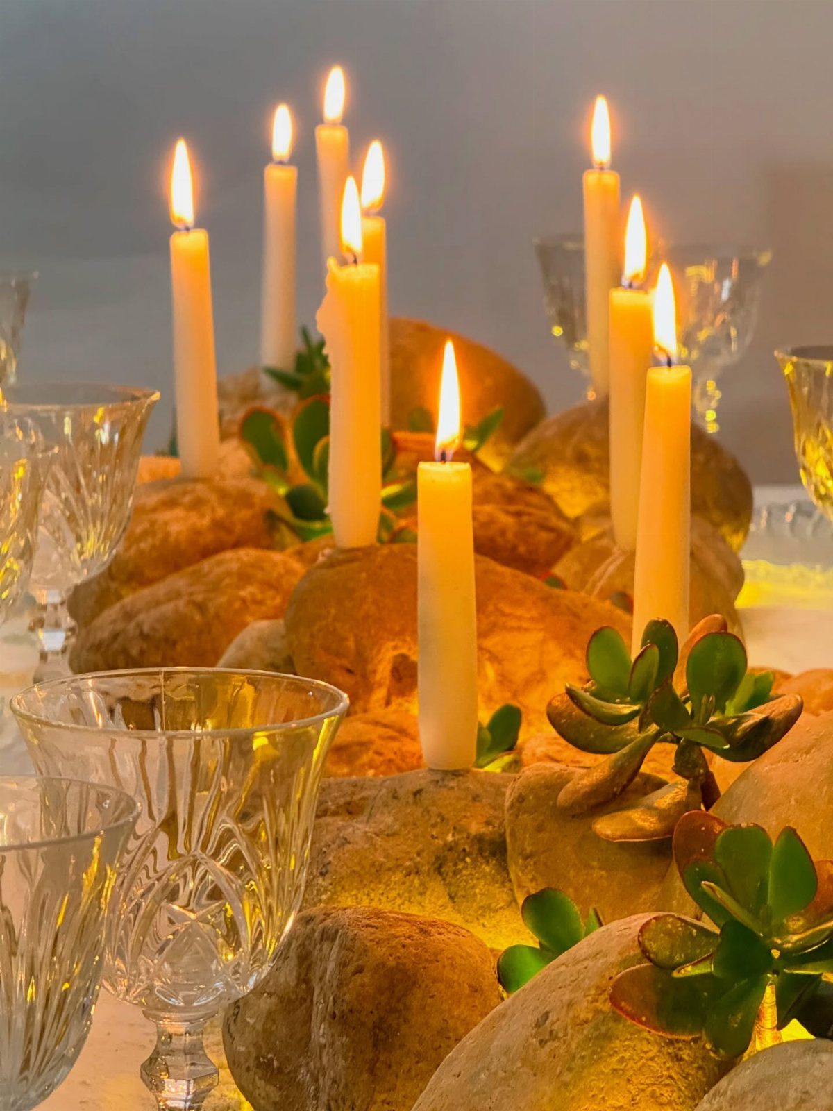 White taper candles and green succulents arranged among river stones as a centerpiece.