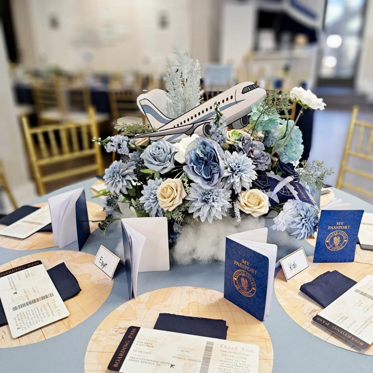 Travel themed centerpiece with blue flowers, a model airplane, and passport place cards.