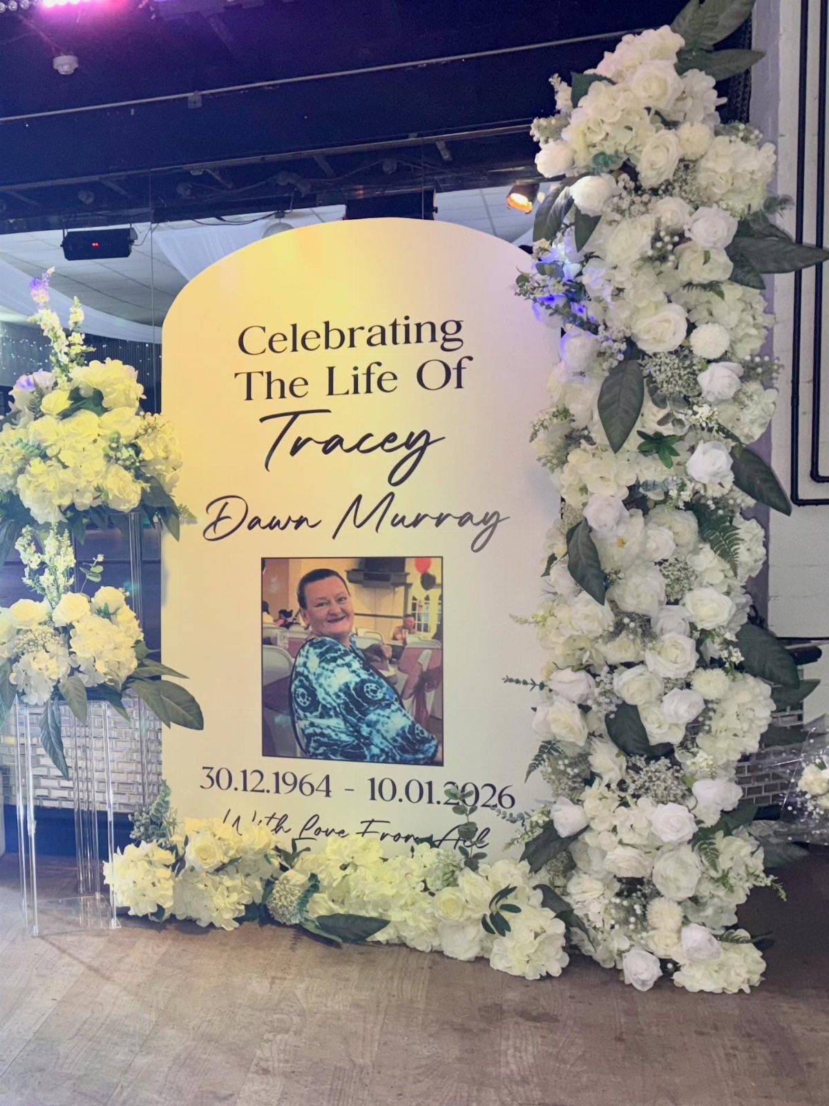 Memorial board with photo and text surrounded by white and yellow flowers.
