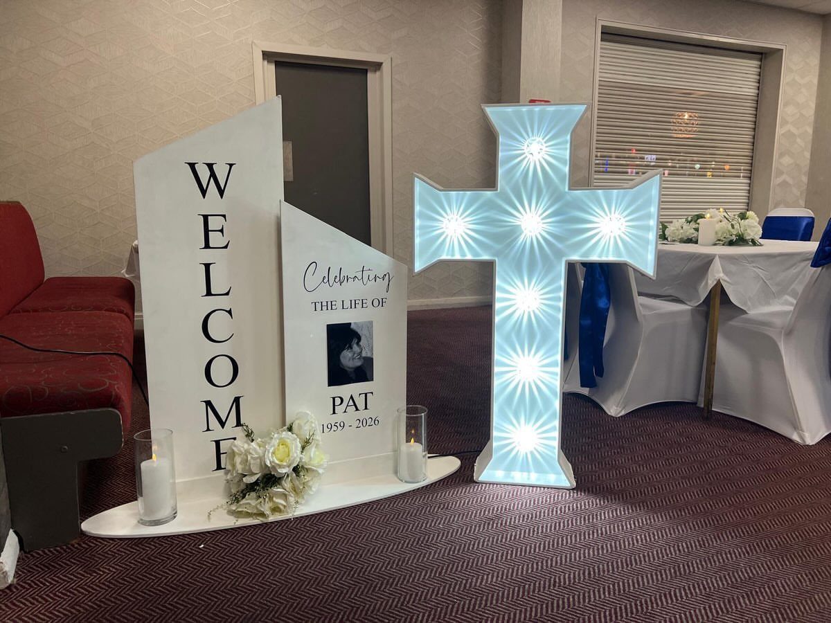 Memorial setup with a glowing white cross, welcome sign, and personalized photo board.