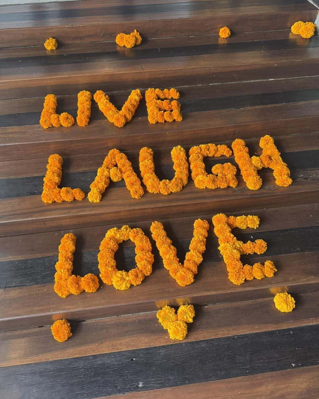 Orange marigold flowers spelling Live Laugh Love on a dark wooden surface.