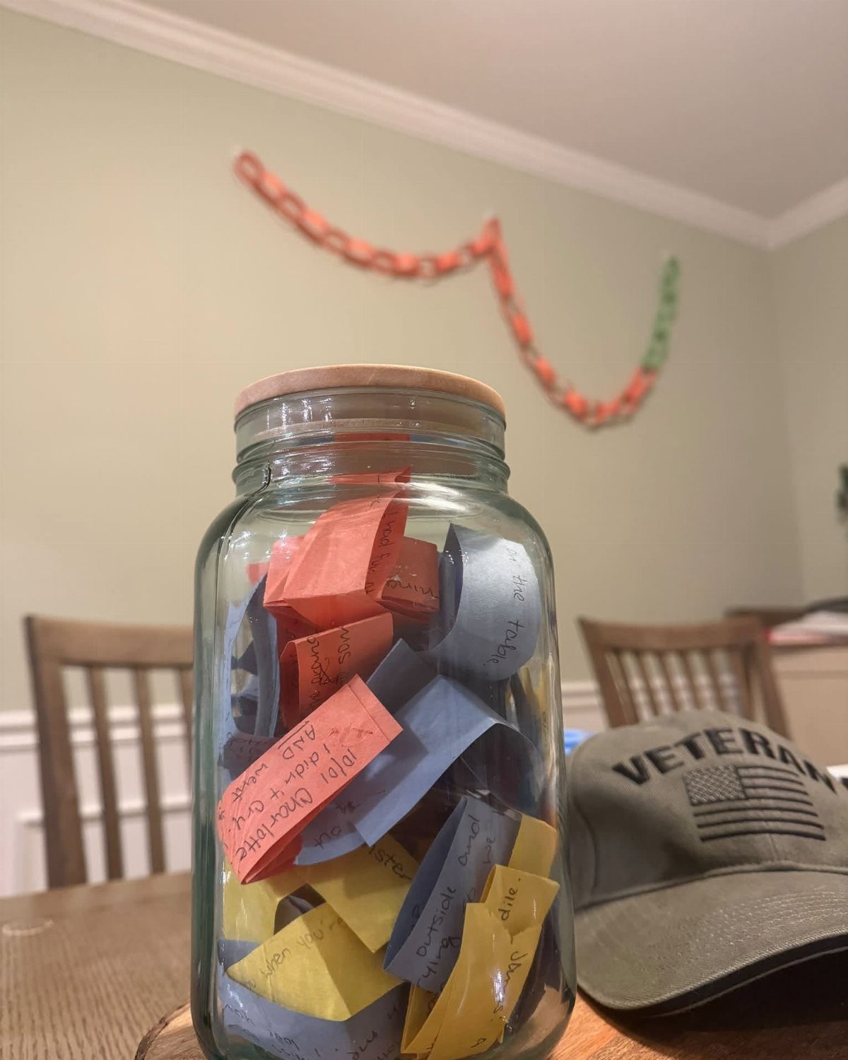 Glass jar filled with colorful memory slips next to a veteran's cap.