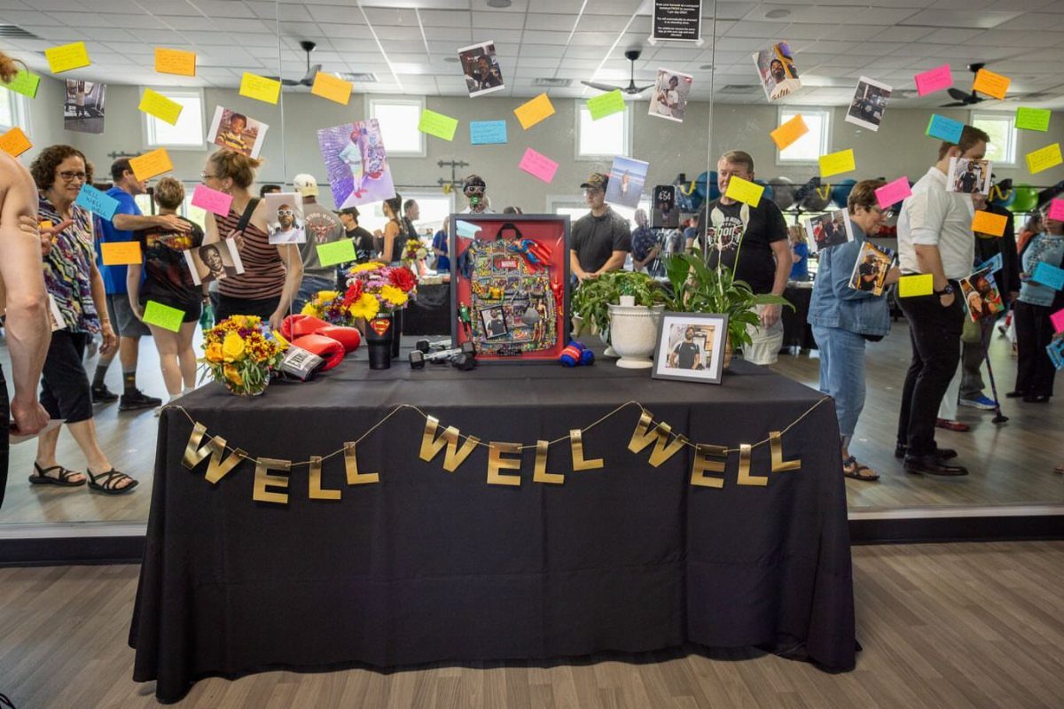 Memorial table with black cloth, gold banner, flowers, and hanging photo display.