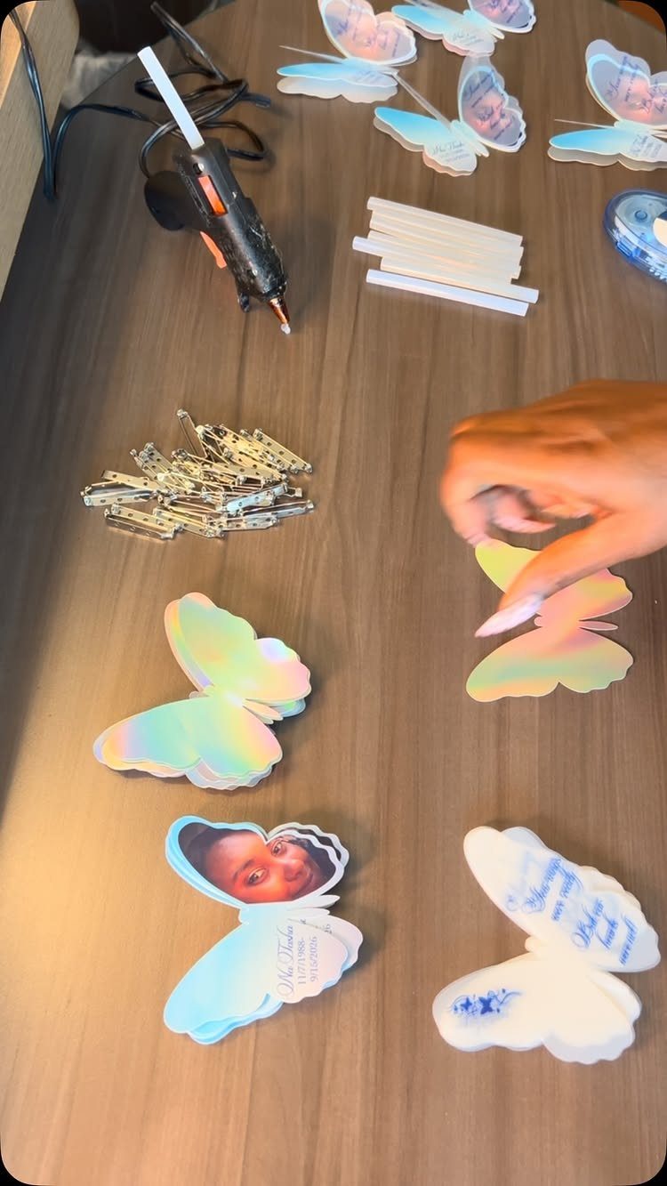 Butterfly-shaped memorial favors with photos being assembled on a wooden table.