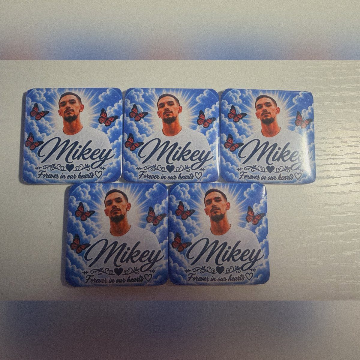 Five square memorial magnets with a man's portrait, clouds, and commemorative text.