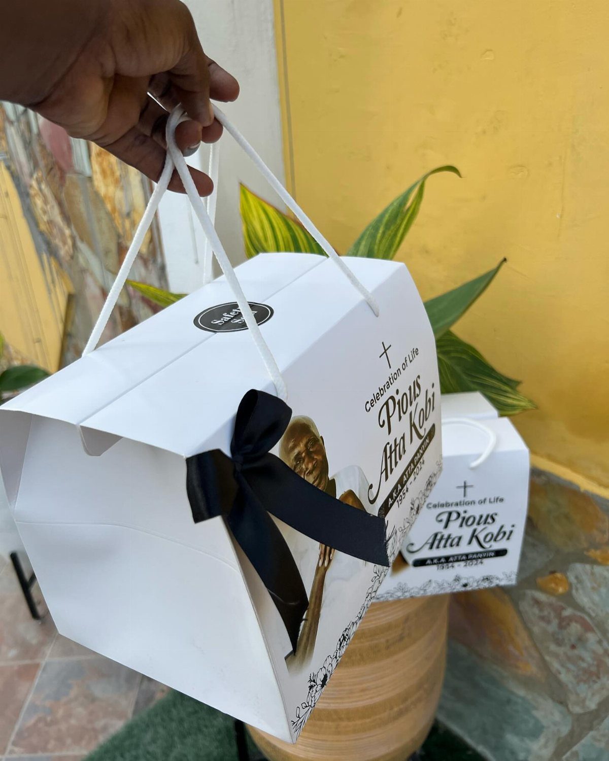 White celebration of life gift bags with black ribbons and memorial photos.