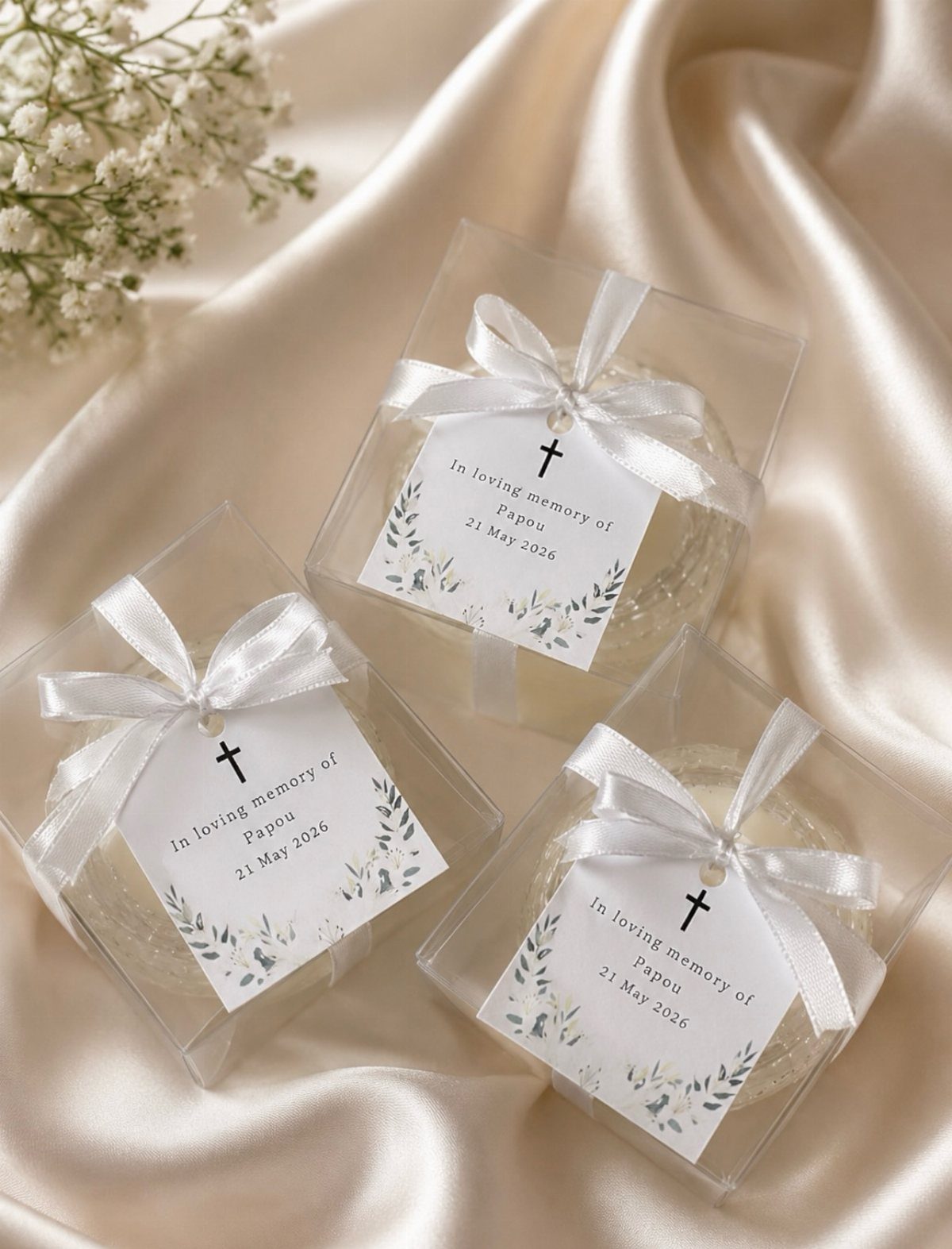 Memorial soap favors in clear boxes with white bows and memorial cards on satin.