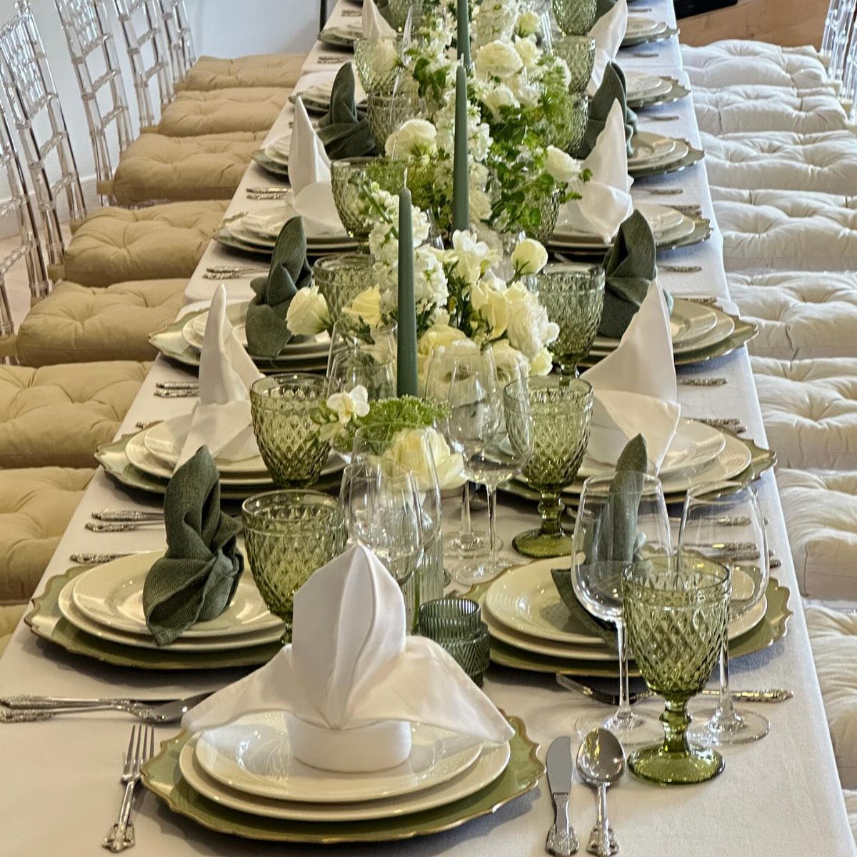 Floral centerpieces with white flowers and green candles on a set dining table.
