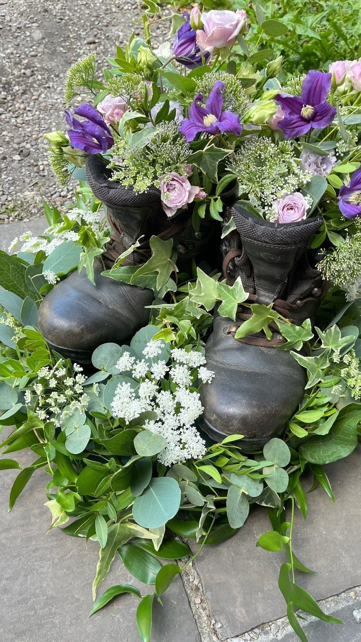 Black leather boots filled with purple and pink flowers and green foliage.