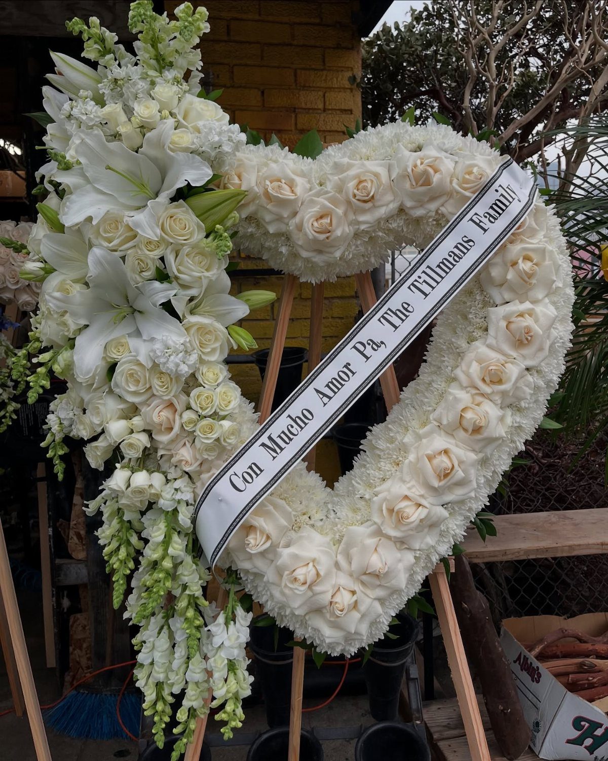 Heart-shaped white rose and lily arrangement with a ribbon on a wooden easel.