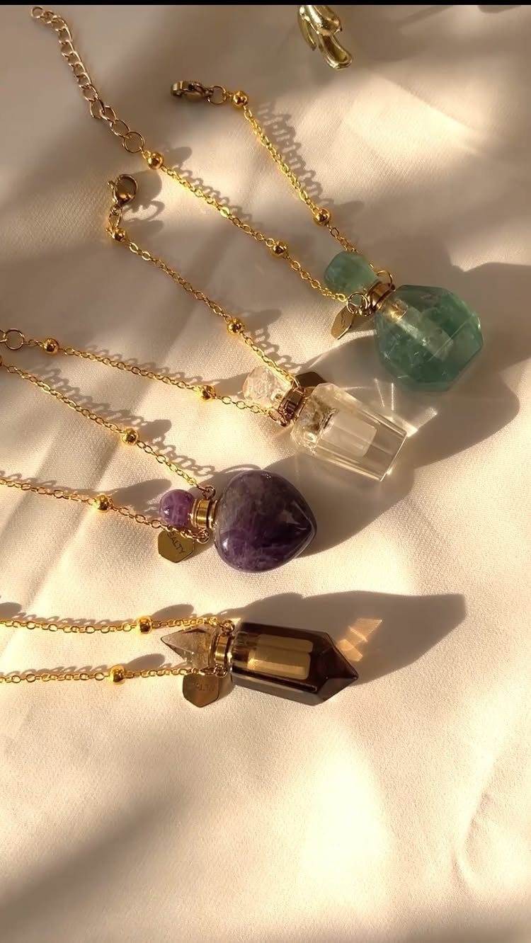 Four gold necklaces with colorful crystal pendants resting on a white cloth surface.