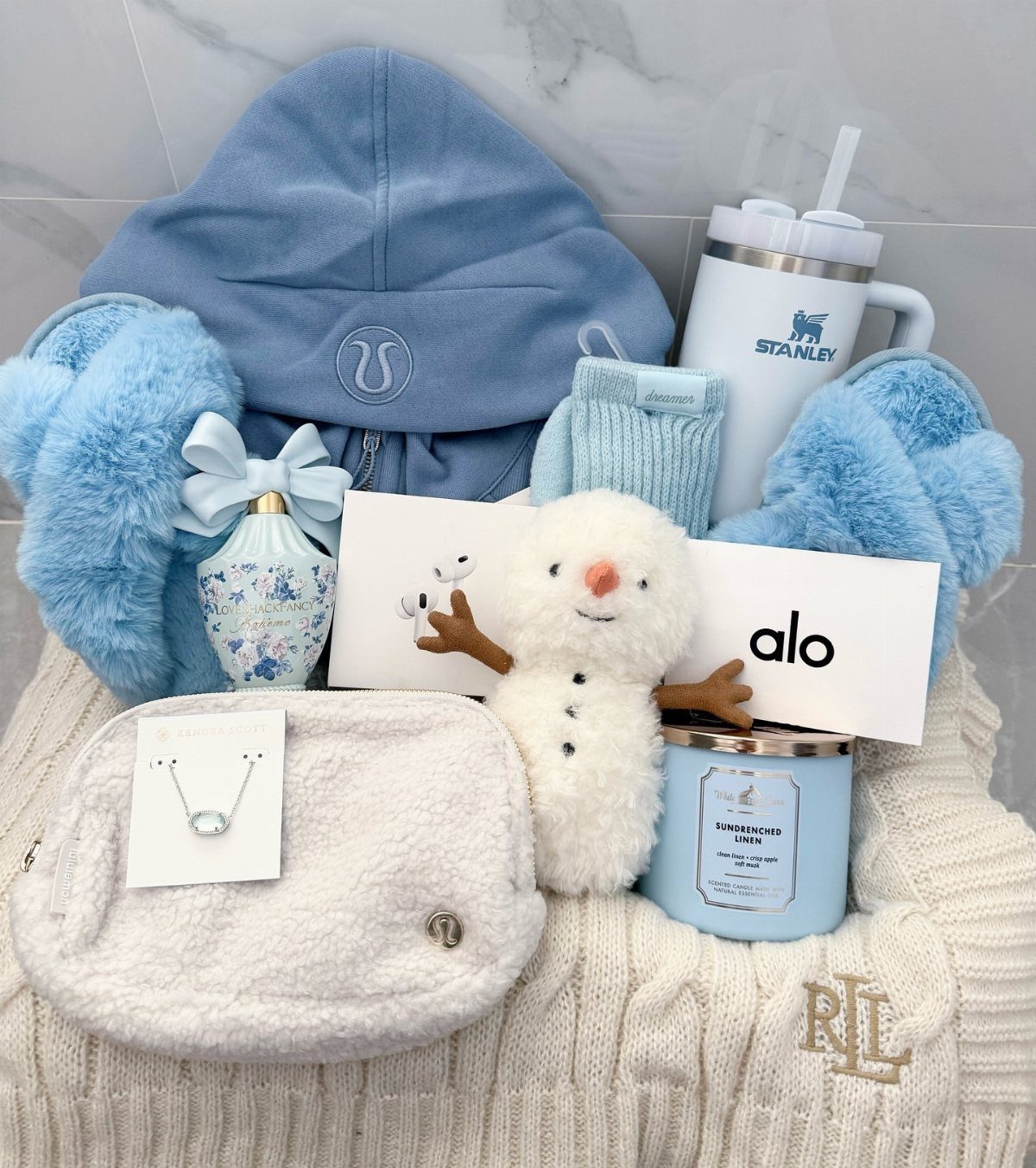 Gift bundle with blue accessories, a white fuzzy belt bag, and a snowman plush.