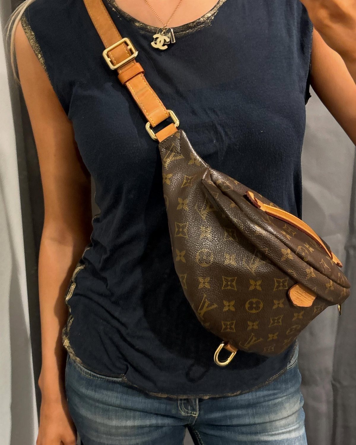 Brown monogrammed belt bag worn across the chest of a person in blue clothing.