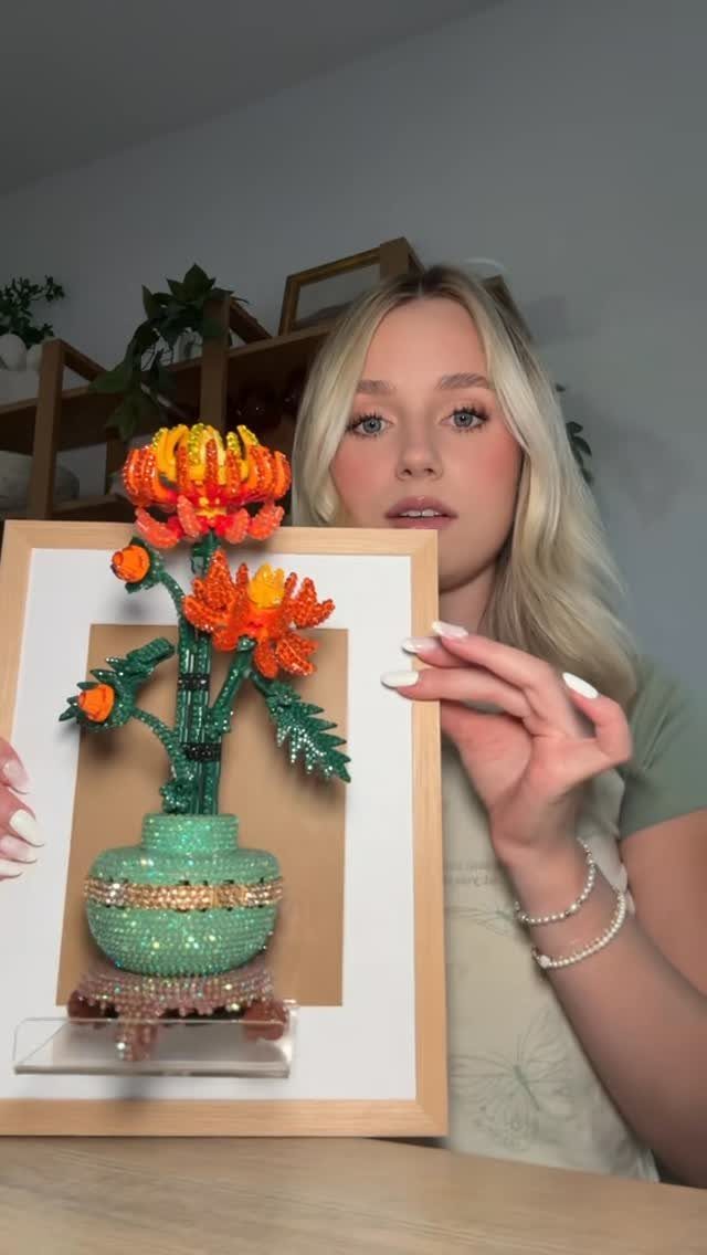 Woman holding a framed 3D bead art piece of orange flowers in a vase