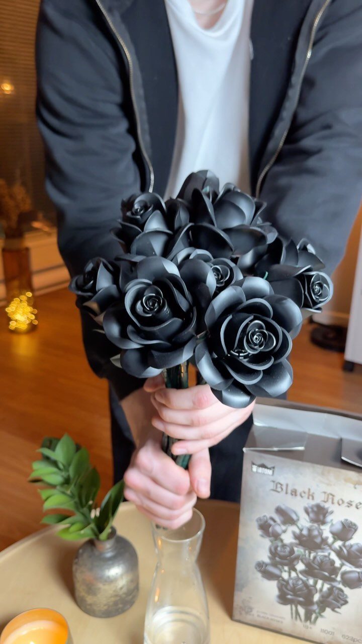 Black artificial roses held by a person over a clear glass vase.
