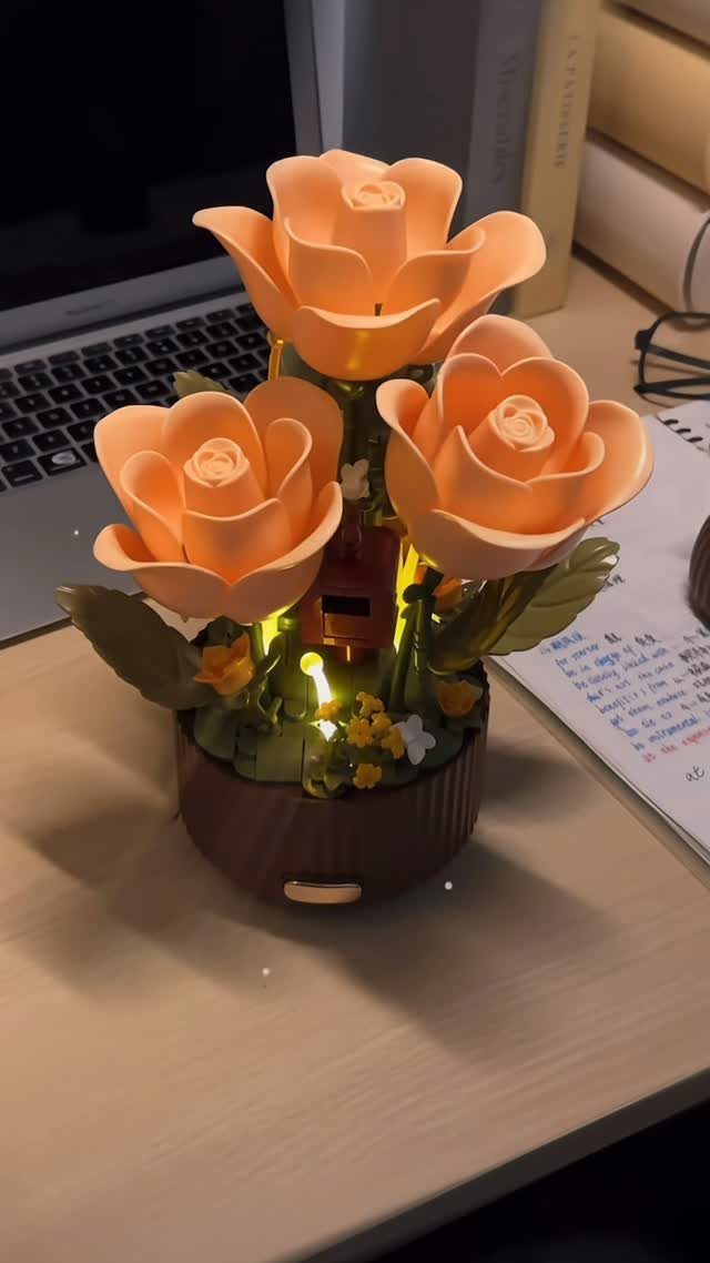 Peach artificial roses in a brown pot illuminated from within on a desk