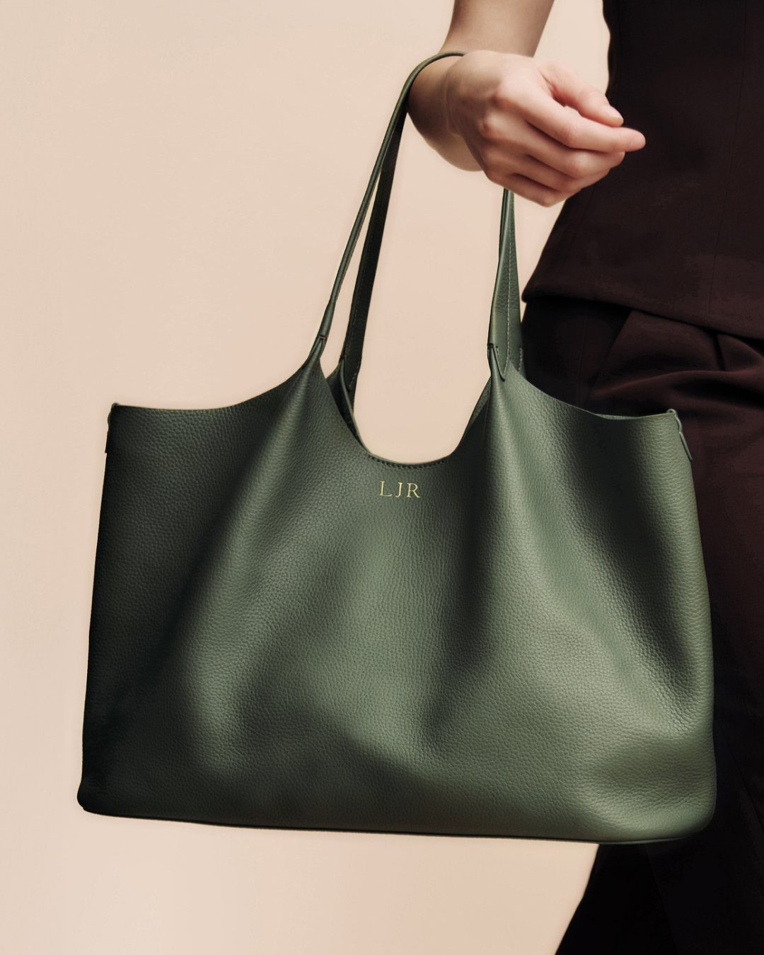 Olive green pebbled leather tote bag with personalized initials held by a person.