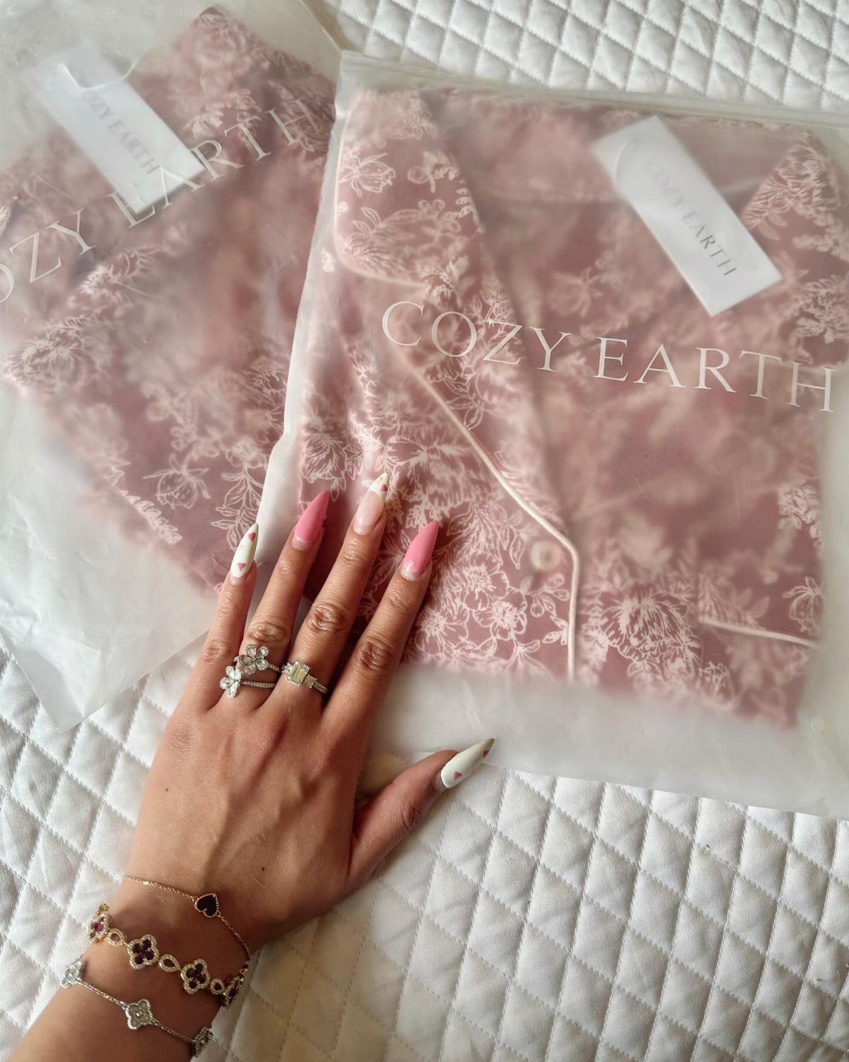Pink floral pajamas in plastic packaging with a hand wearing jewelry resting on top.