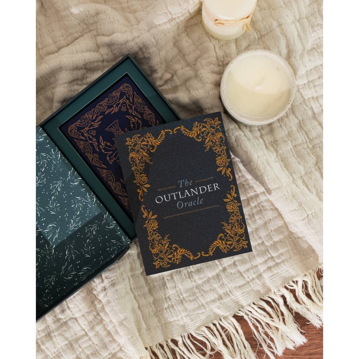 The Outlander Oracle book with gold detailing on white textured fabric with candles.