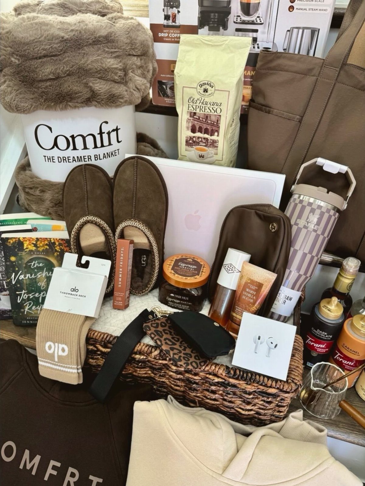 Gift basket with brown loafers, fluffy blanket, tote bag, and various skincare products.