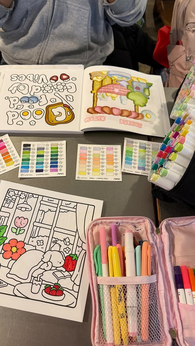 Coloring book and pink marker case with colorful pens on a grey table.