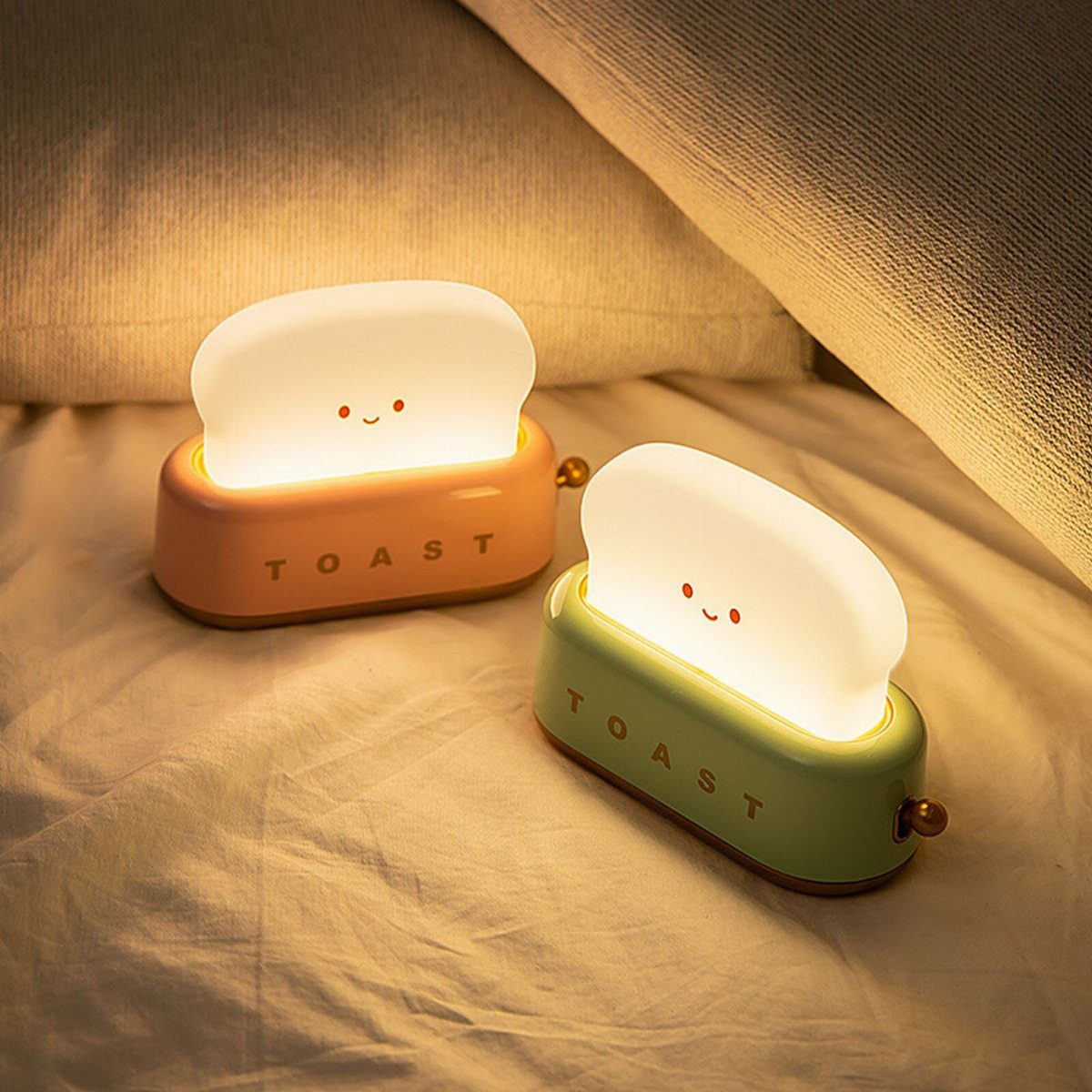 Two toast-shaped LED night lamps glowing on a white bedsheet.