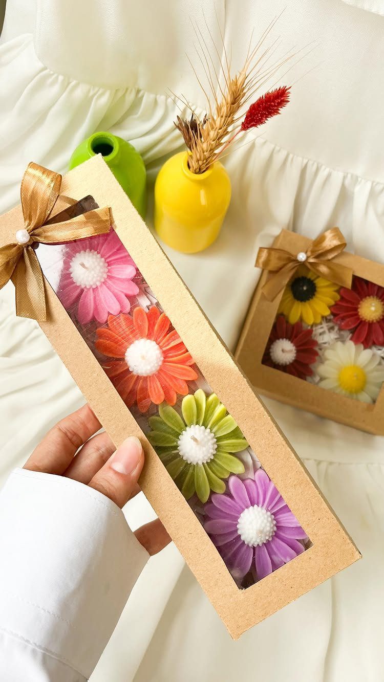 Flower-shaped colorful candles in a brown gift box held by a person