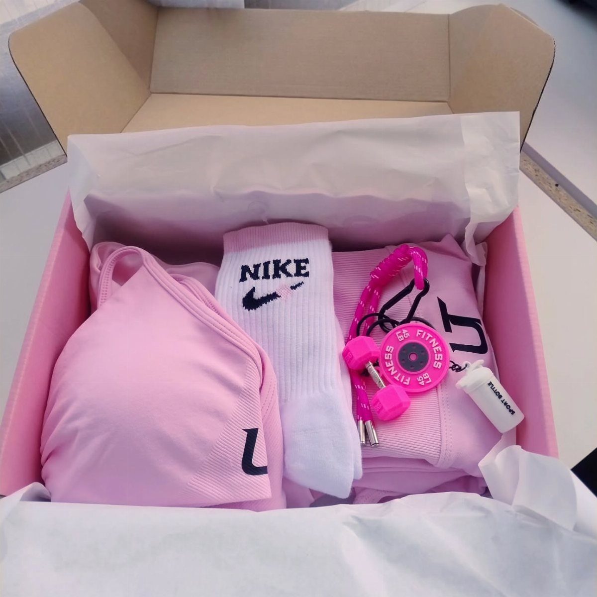 Pink fitness gear set including sports bra, socks, and dumbbells in a gift box.