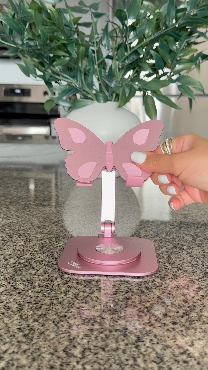 Pink butterfly-shaped phone stand held by a hand on a granite countertop.