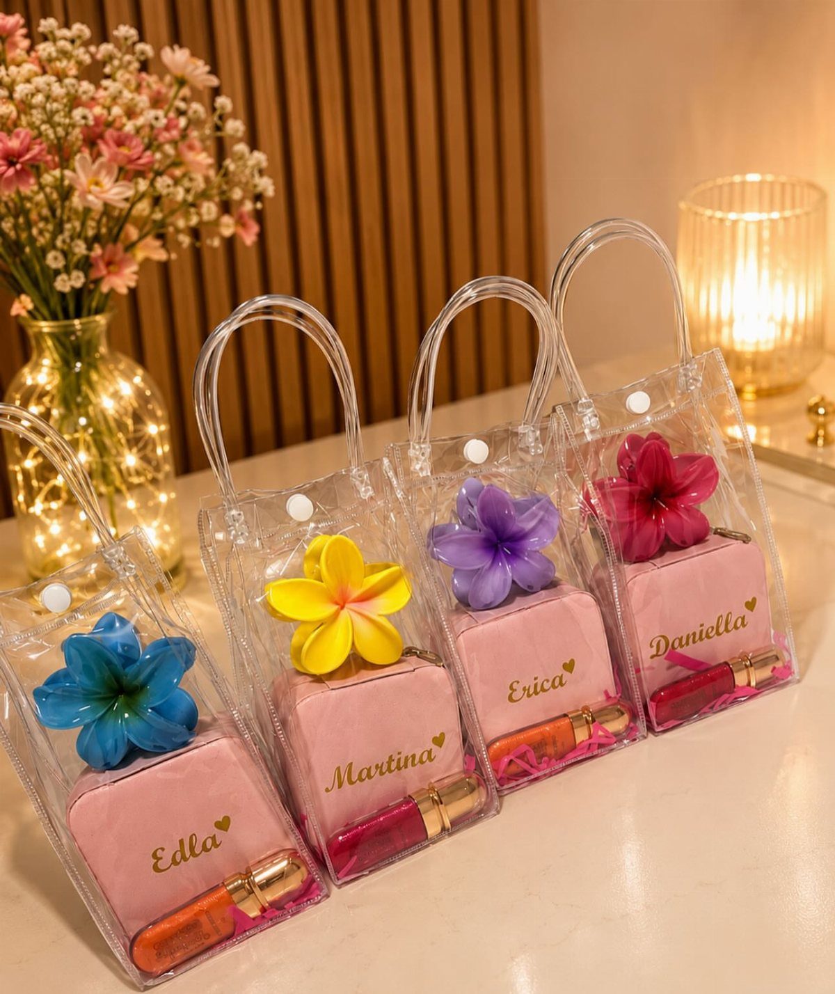 Four clear gift pouches containing pink pouches, lipsticks, and colorful artificial flowers.