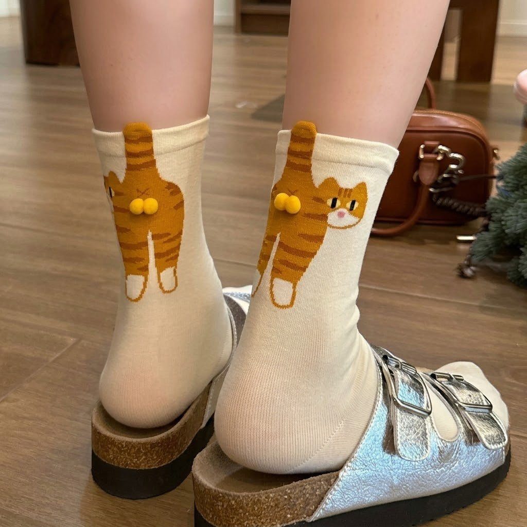 White crew socks with orange tabby cat designs and yellow pom-pom eyes.