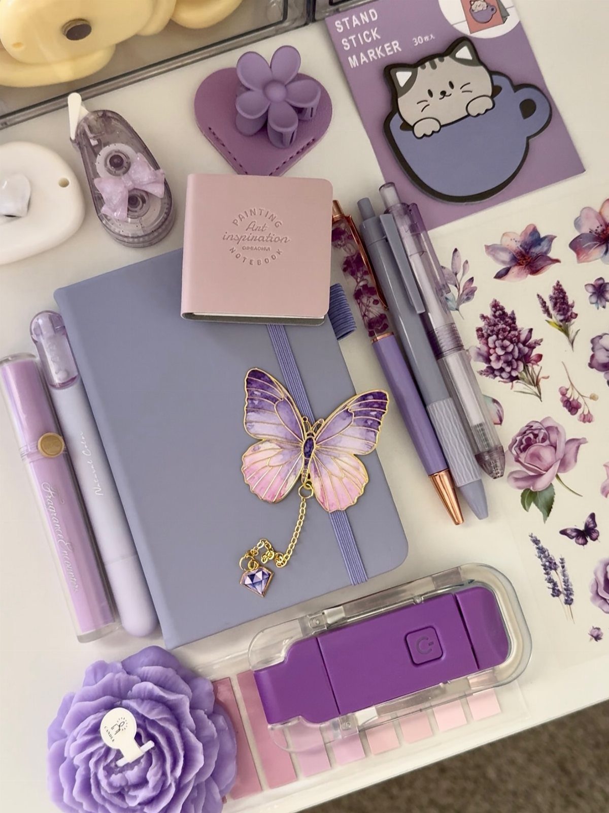 Purple stationery set featuring a notebook with butterfly charm, pens, and floral stickers.