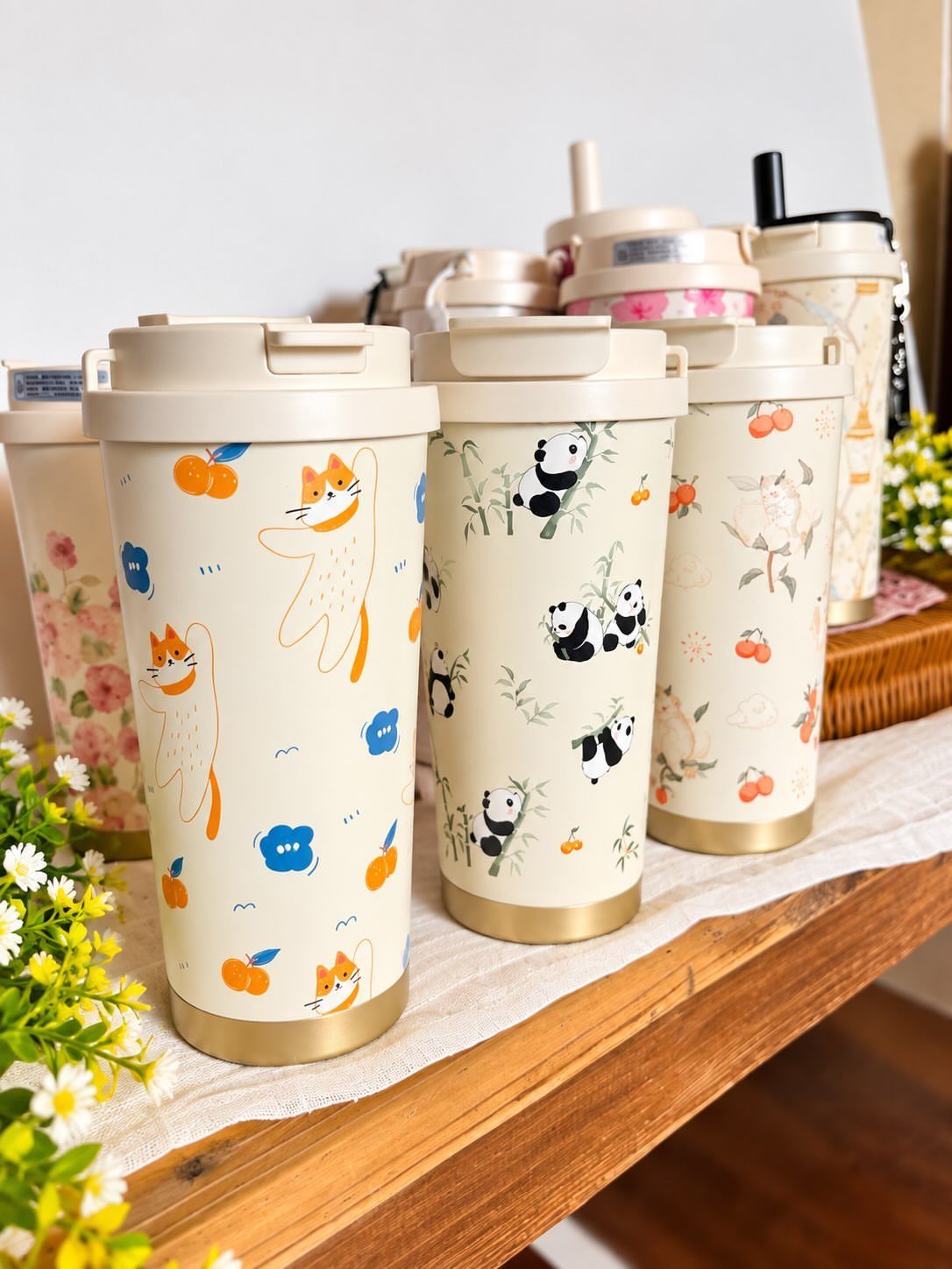Cream-colored travel mugs with cute animal illustrations on a wooden table.