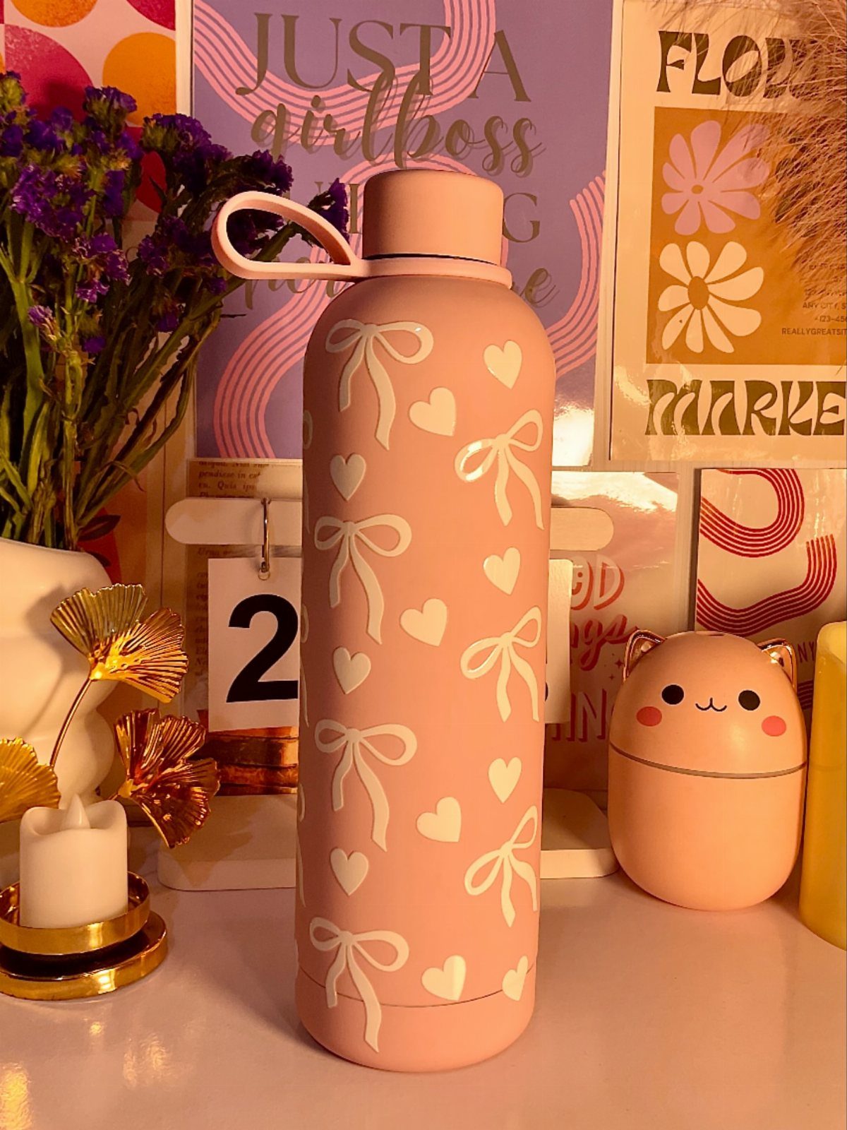 Pink water bottle with white hearts and bows surrounded by cute desk accessories.