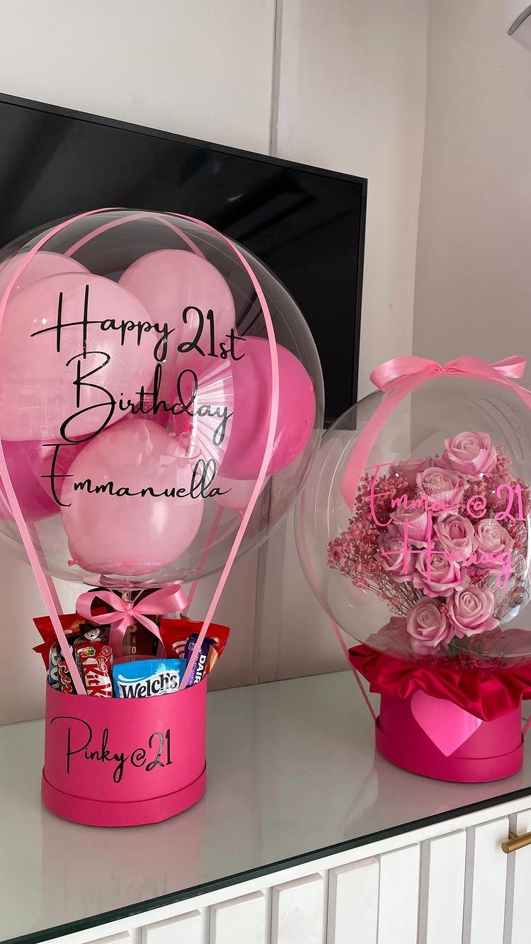 Two pink birthday gift arrangements with clear balloons, candy, and pink roses.