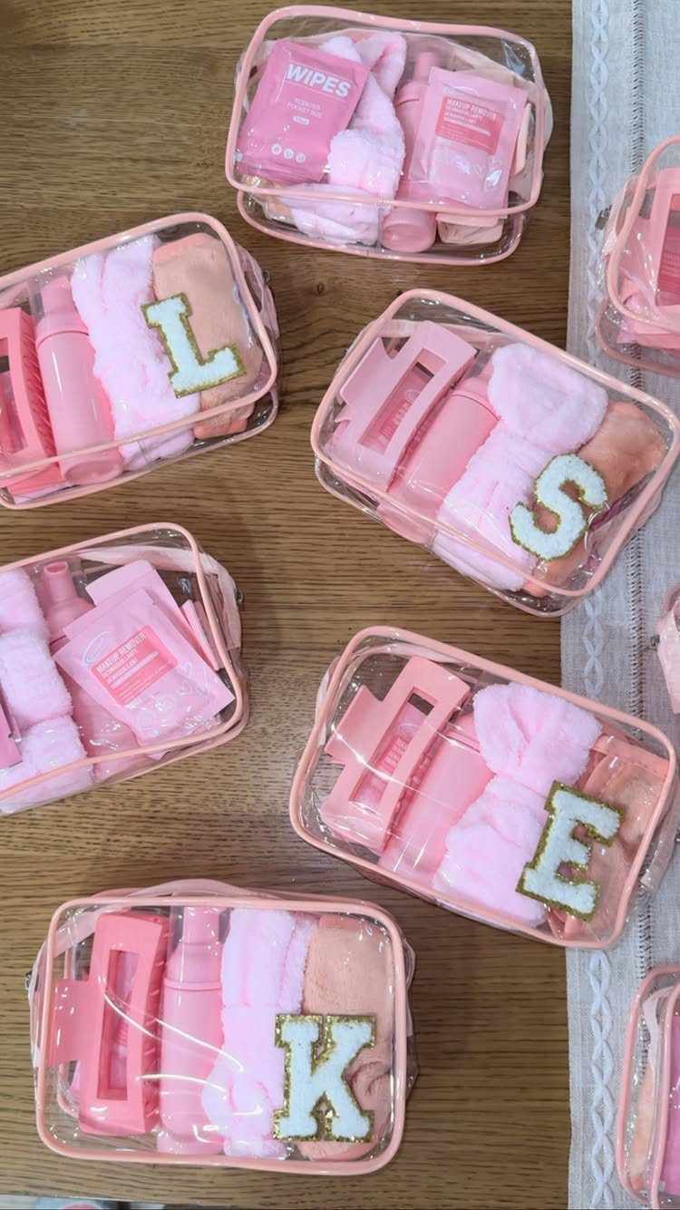 Pink spa kits in clear pouches with glitter letters on a wooden table.