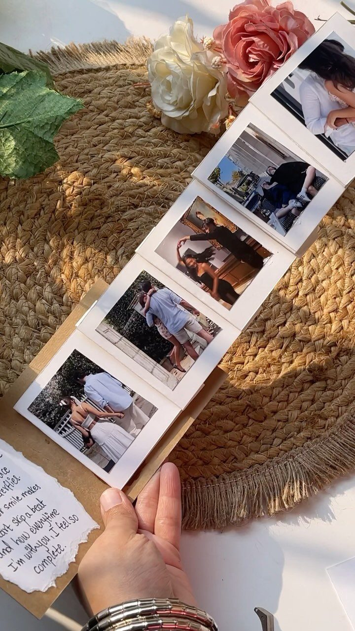 Handmade accordion photo album with couple photos resting on a woven straw mat.