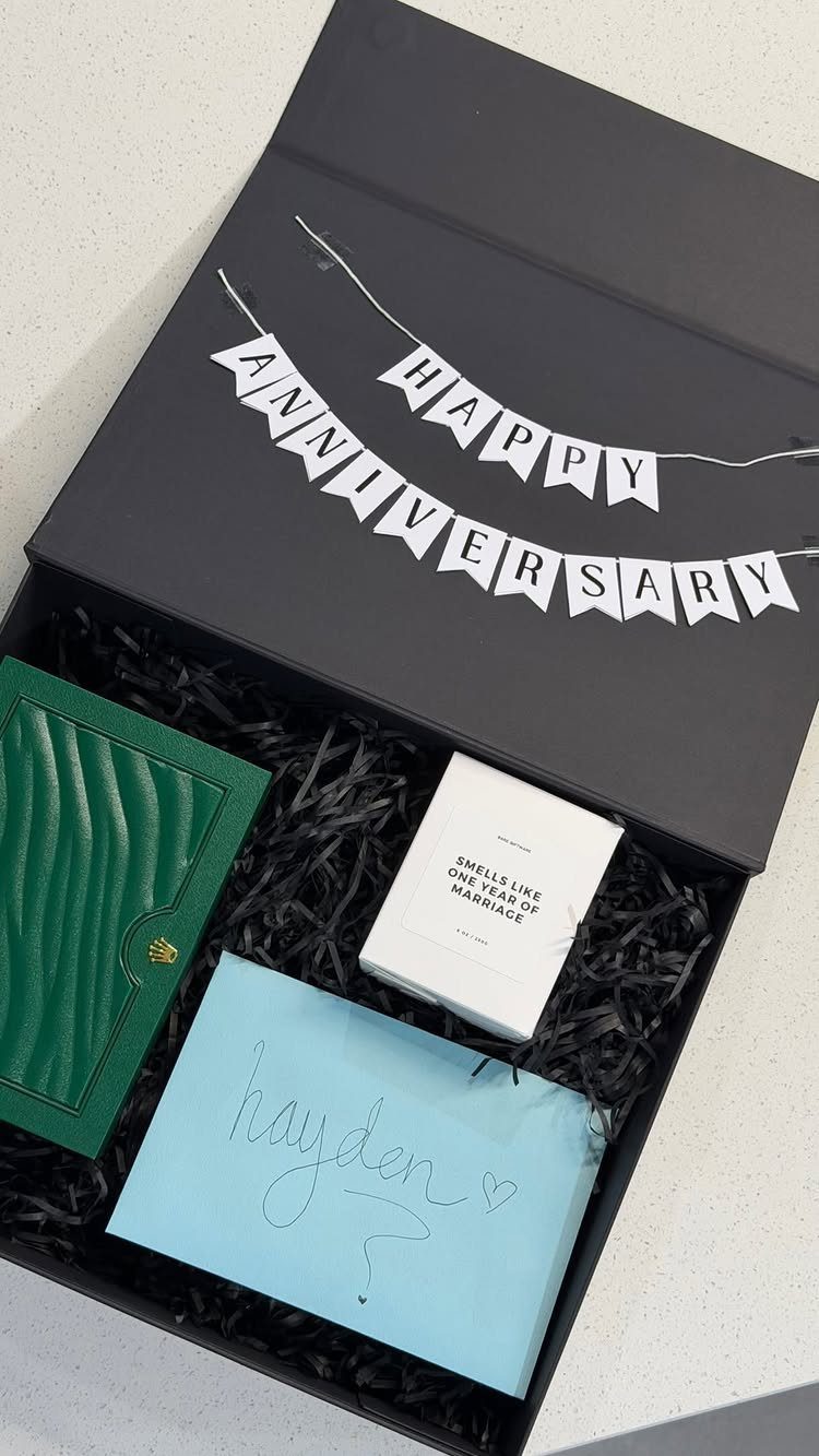 Anniversary gift box with a green notebook, white candle, and blue handwritten envelope.