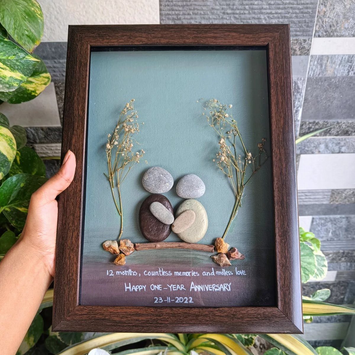 Framed stone art depicting a couple hugging with anniversary text and dried plants.