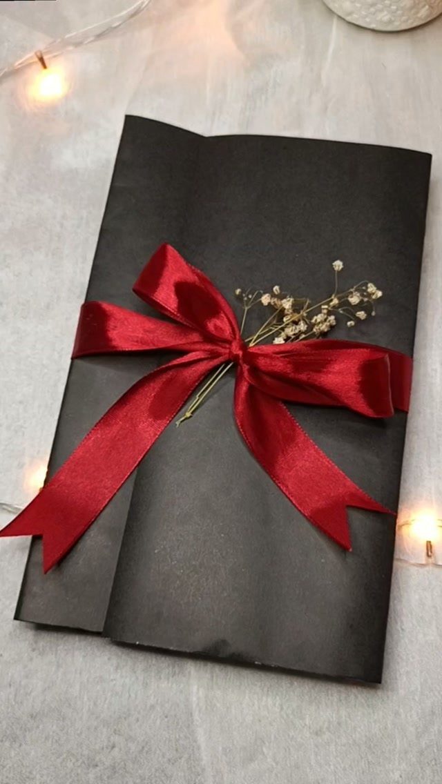 Black envelope tied with a red satin bow and dried white flowers.