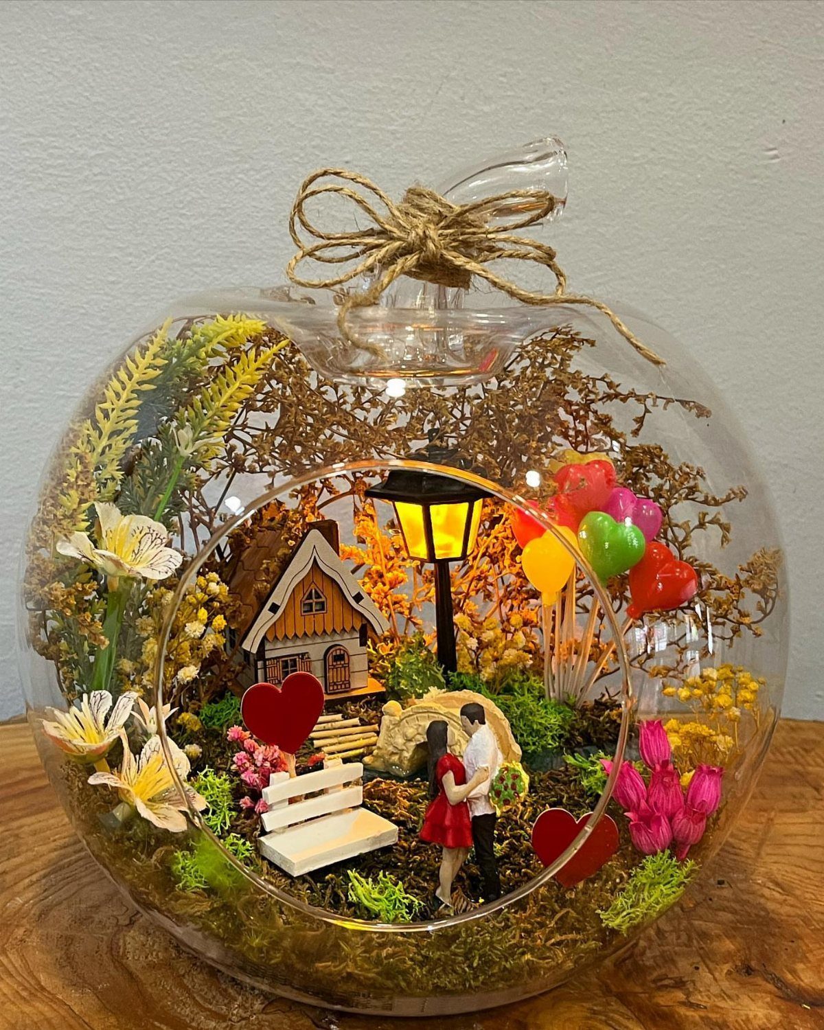 Miniature romantic scene inside a glass globe with a couple and red hearts.