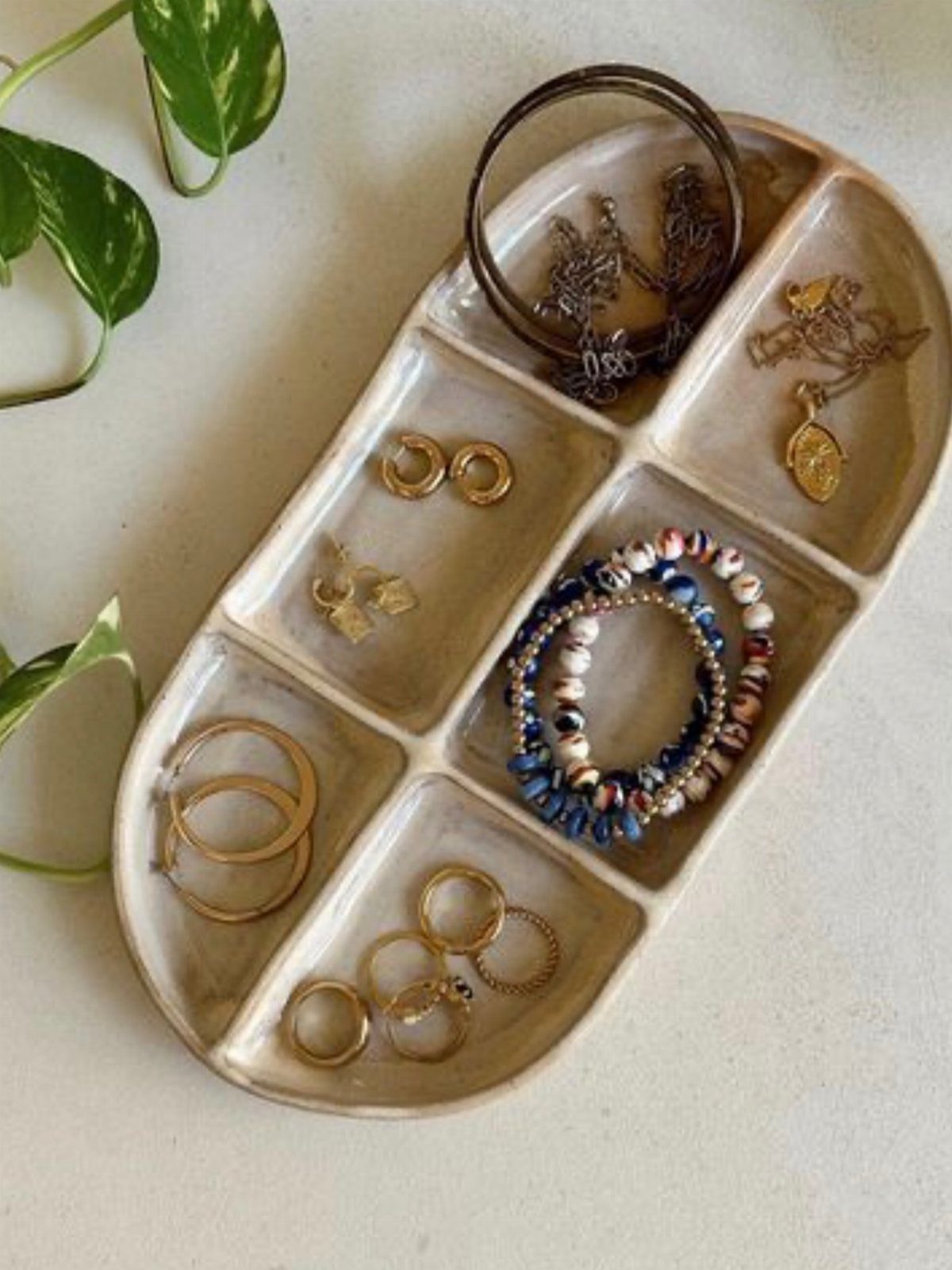 Beige clay jewelry bowl with multiple compartments holding rings, necklaces, and beaded bracelets.