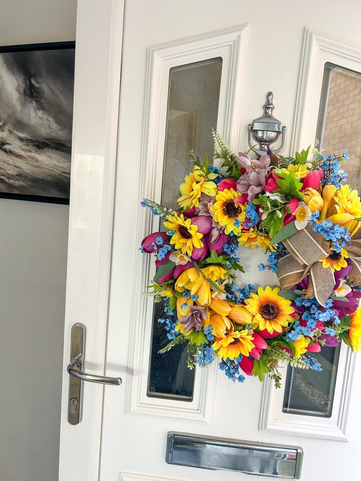 Colorful floral wreath with sunflowers and a burlap bow hanging on a white door