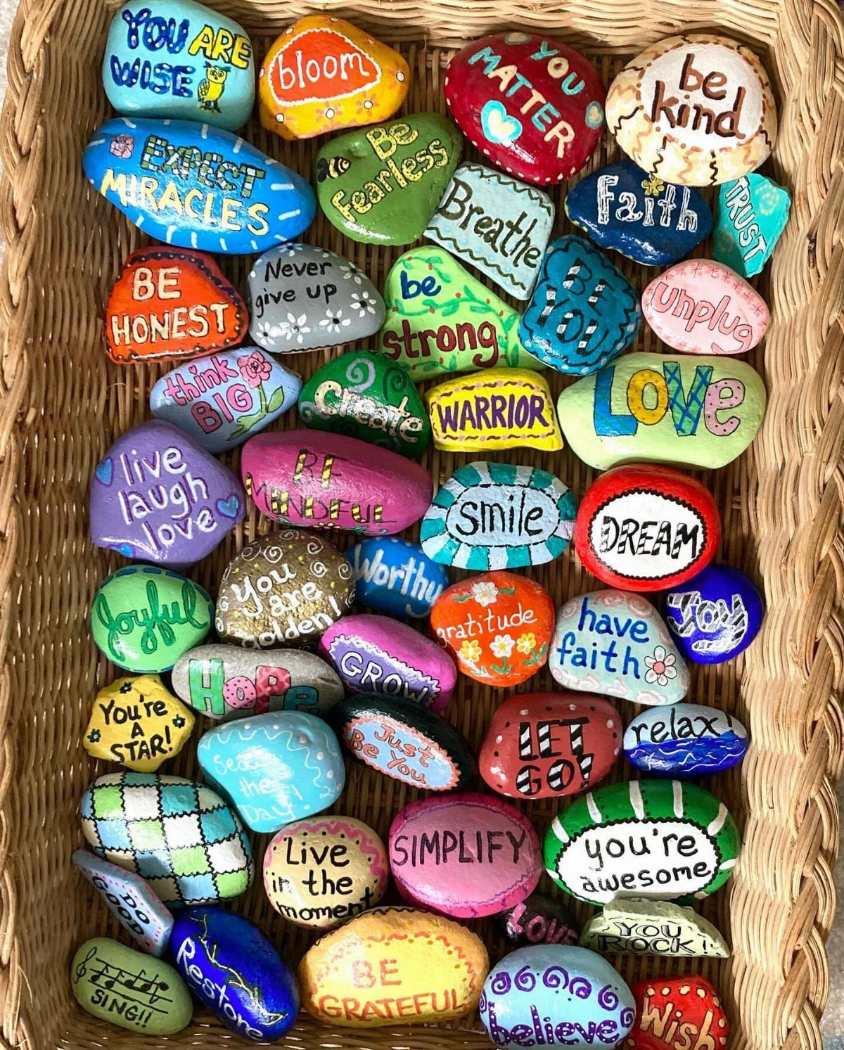 Colorful painted rocks with inspirational words and phrases arranged in a wicker basket.